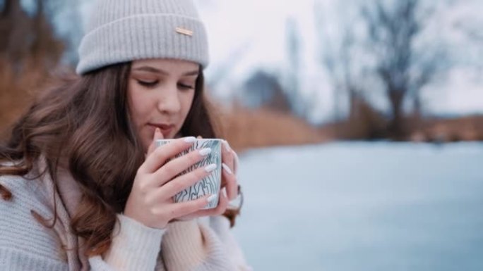年轻女子坐在冰冻的湖上喝热茶