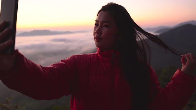 剪影年轻女子在山上用阳光和雾拍摄风景。独自旅行背包客带着相机徒步旅行。假日旅行和度假概念。