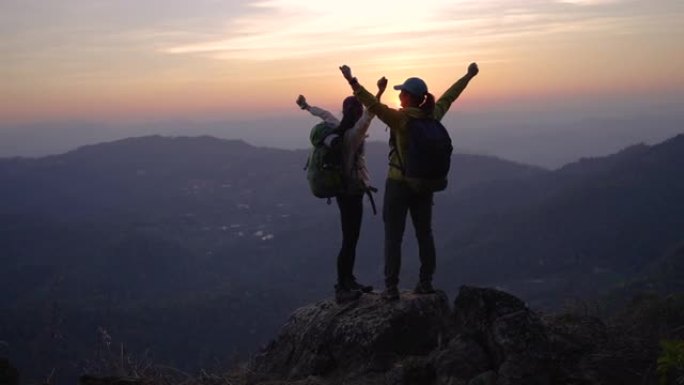 两个女人徒步上山，在山顶上击掌，举手庆祝成功