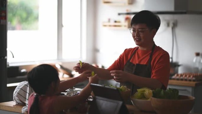 西安中国母亲在厨房柜台做饭，并与女儿一起使用数字平板电脑从互联网上学习食物