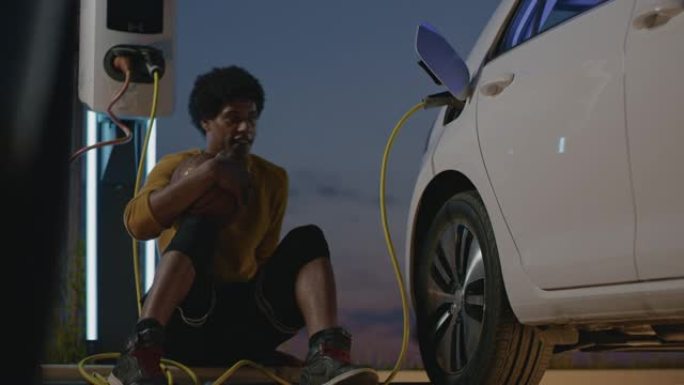 SLO MO年轻篮球运动员晚上在停车场为电动汽车充电