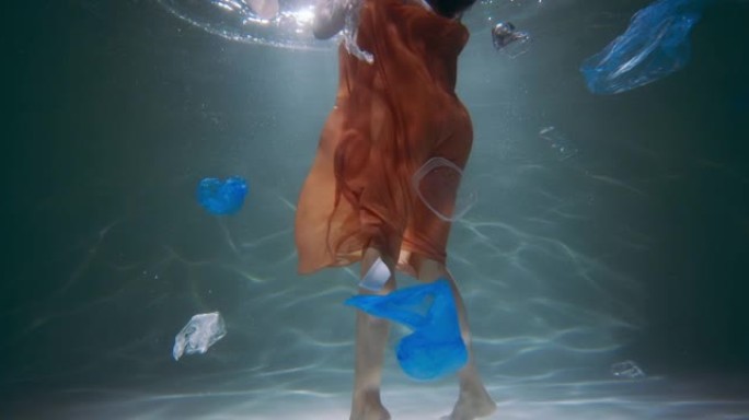 粗心塑料污染的电影概念。女性的腿站在水下，各种废物漂浮在慢动作周围。