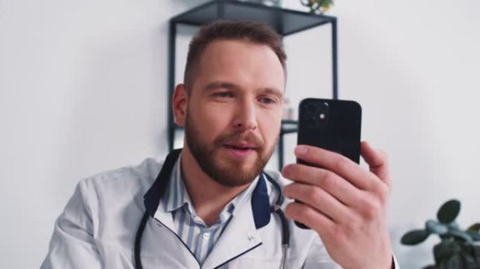 快乐的年轻男性医生在办公室使用智能手机视频通话聊天应用程序在自我隔离上咨询远程患者。