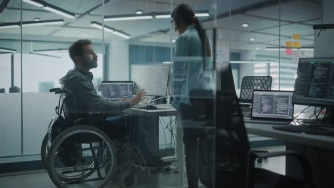 残障友好的办公室: 快乐的IT程序员在轮椅上与同事交谈，同时在计算机上工作。软件工程师开发创新的应用