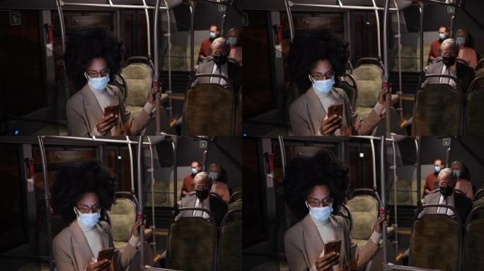 在公共汽车上戴着covid面具的非裔美国女商人拿着智能手机