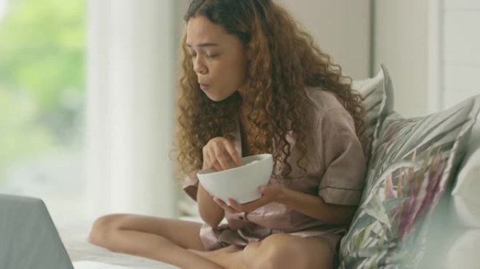 4k视频片段，一名年轻女子使用笔记本电脑并在家中床上吃爆米花