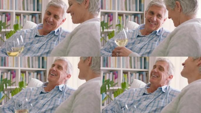 老年夫妇在他们现代房子的客厅沙发上喝香槟或葡萄酒。退休时快乐、积极、大笑的老年人，在家里的沙发上享受