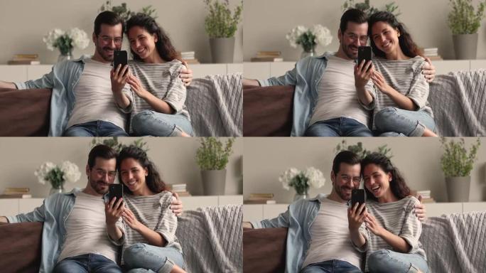 恋爱中的美丽夫妇用智能手机拥抱在沙发上