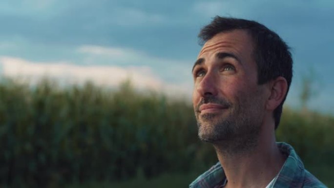 快乐的人在一片绿色的玉米田里微笑着环顾四周。英俊的中年男性农民欣赏美景，感谢好天气，对他的农作物和生