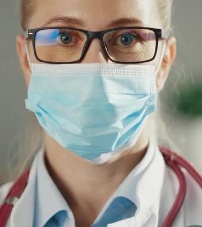 一位经验丰富的女医生在办公室穿着白大褂和一次性口罩的垂直肖像。医疗保健专业人员或戴眼镜的护士长看着相