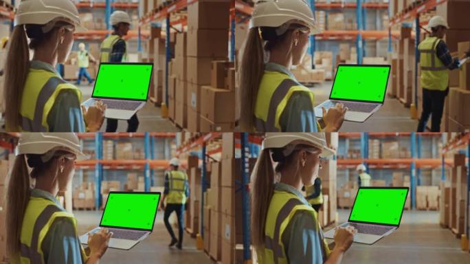 专业女工戴着安全帽拿着带绿色色度键屏幕的笔记本电脑，在摆满了货架的零售仓库中，在风景模式下摆满了送货