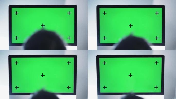 男人在绿屏的台式计算机上看的后视图，相机向上移动