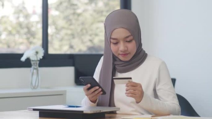 亚洲穆斯林女士使用电话，信用卡在办公室购买和购买电子商务互联网。