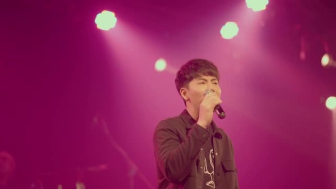 年轻的亚洲摇滚歌手在空旷的舞台和多色的聚光灯下唱歌。