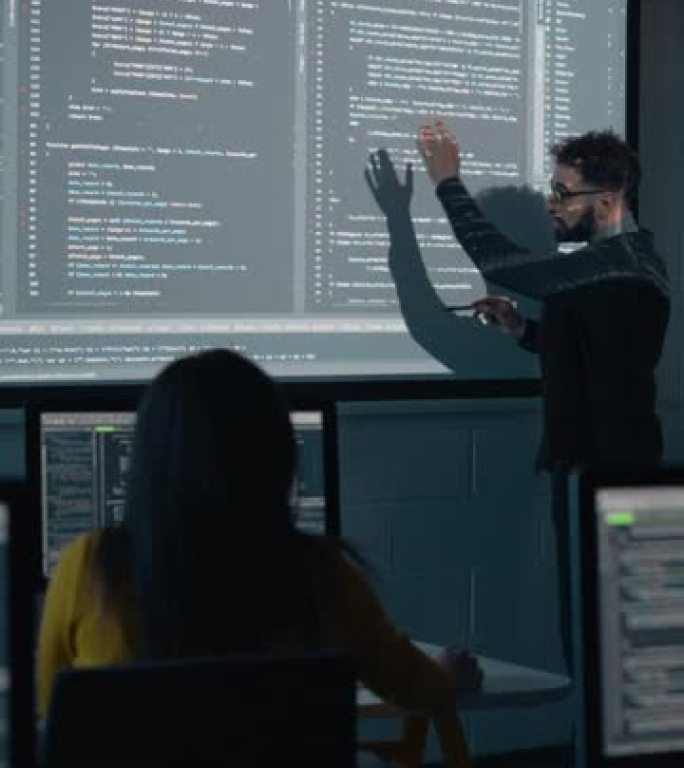 垂直屏幕: 老师在黑暗的大学教室里为不同的多种族学生提供计算机科学讲座。用编程代码投影幻灯片。解释信