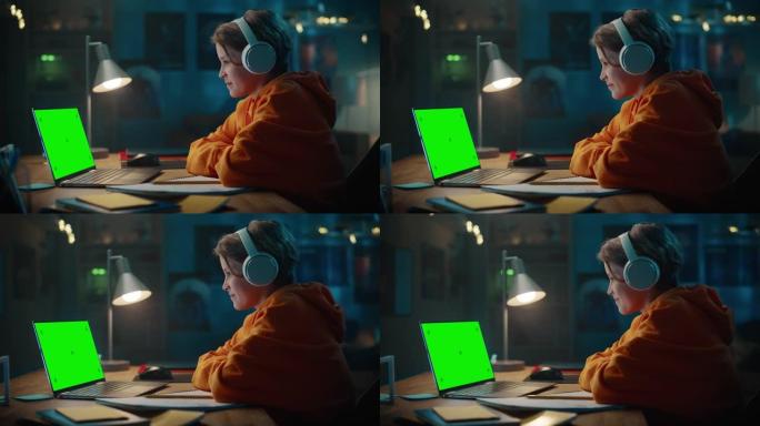 戴着耳机的聪明小男孩在带有绿屏显示的笔记本电脑上观看教育视频。快乐的青少年浏览教育研究，在笔记本上写