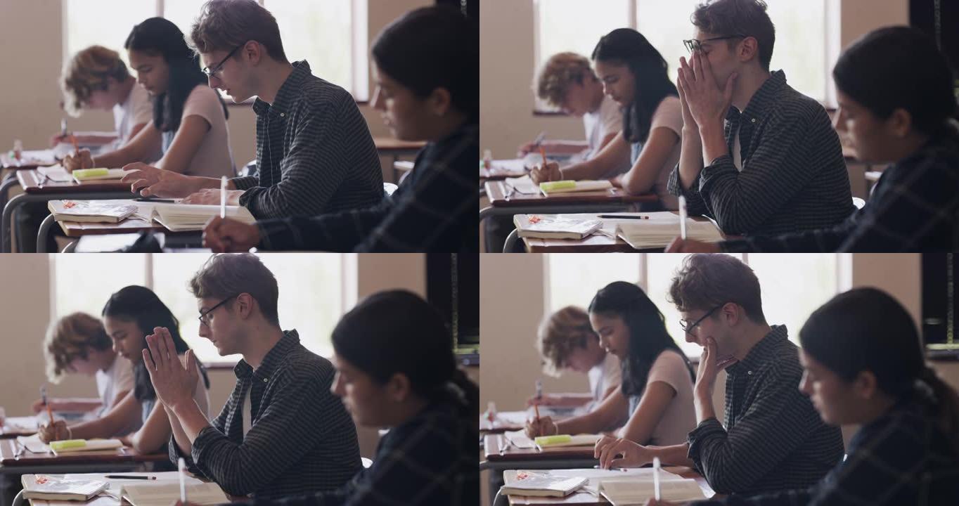 4k视频片段，一个十几岁的男孩在高中的教室里在办公桌前写字时看起来压力很大
