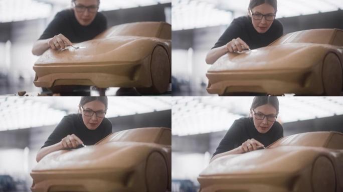女性汽车建模师在由橡皮泥造型粘土制成的概念车上享受创造性的工作过程。美丽的设计师使用刮铲来平滑现代电