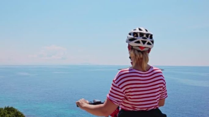 金发碧眼的骑自行车的女人在赫瓦尔岛 (Hvar island) 海岸休息，看着海上的一个小岛，上面有