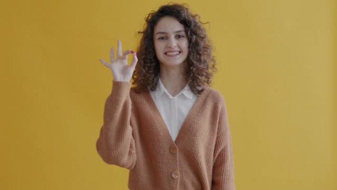 满意的年轻女士肖像，表现出良好的手势，并在黄色背景上微笑