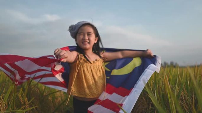 马来西亚独立日一名亚洲华裔年轻女孩在padi球场上裹着马来西亚国旗，享受着早晨的阳光，感到自豪和幸福