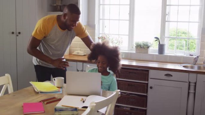 非裔美国女儿和她的父亲在厨房的桌子上一起使用笔记本电脑