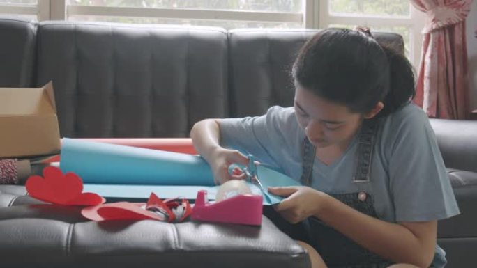 亚洲年轻少女制作手工物品护理包通过切割一张红纸准备从远处发送给她的家人或朋友。