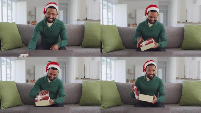 男子戴着圣诞老人的帽子打开礼品盒，同时在笔记本电脑上进行视频聊天