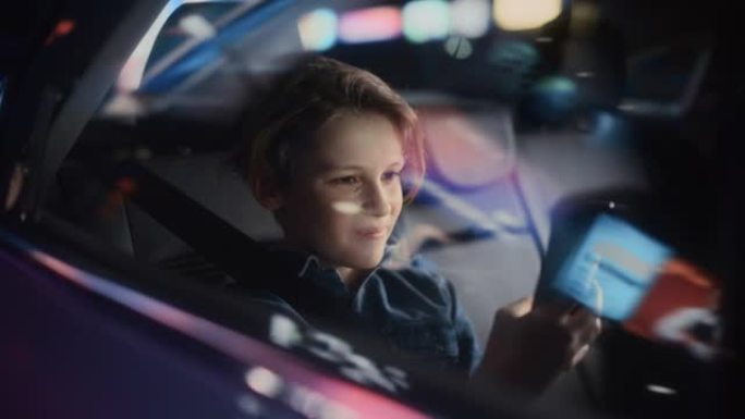 小男孩坐在汽车后座上，晚上通勤回家。乘客在带有工作霓虹灯的城市街道上乘坐出租车时，在智能手机上观看有
