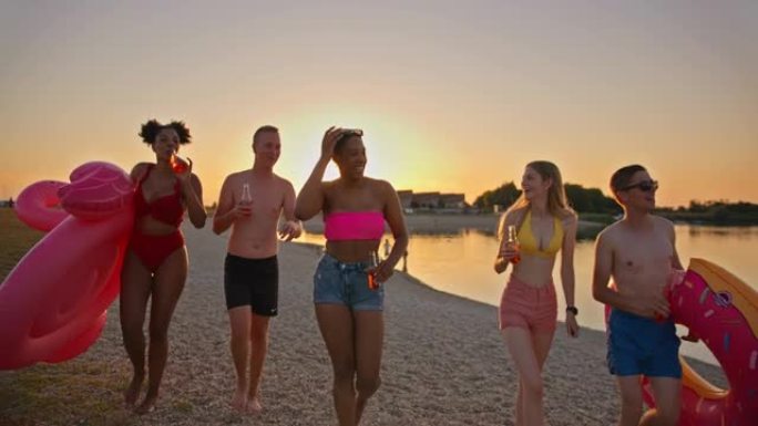 SLO MO年轻人在日落时在海滩上喝酒和散步很有趣