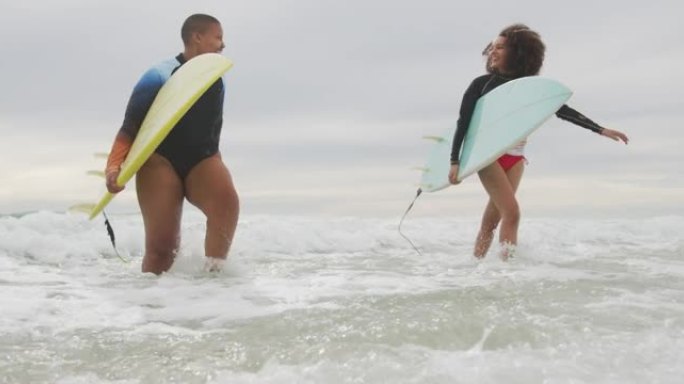 快乐的非洲裔美国女性朋友抱着冲浪板跑出大海