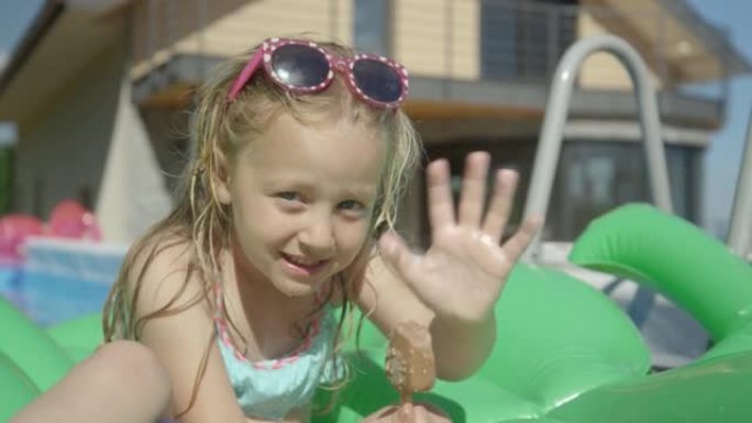 特写: 可爱的小女孩，在游泳池里放着冰淇淋吧，向相机挥手