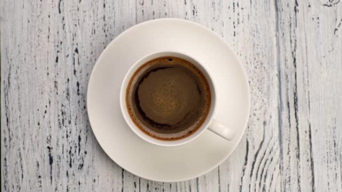 完美的早餐。白色杯子中的黑色泡沫咖啡在木制垃圾背景上。俯视图