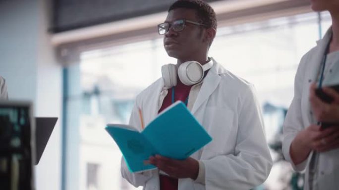 年轻的黑人男性工程专业学生在实验室提问和做笔记的慢动作肖像。实验室助理在会议上展示主动性和给出想法，