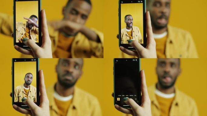 美国黑人男子做鬼脸为手机相机摆姿势，同时手触摸屏幕拍照