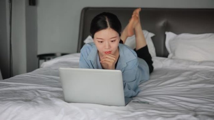 使用笔记本电脑躺在床上的年轻女性