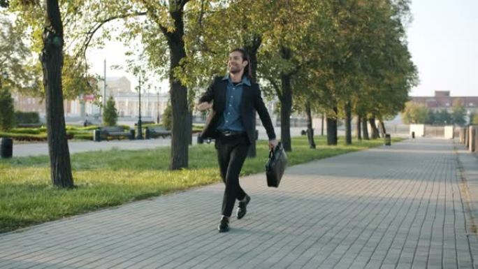 成功的年轻商人带着手提箱在城市中行走，然后跳着跳舞