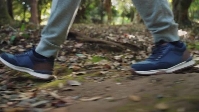 一个人在森林公园大自然中背包旅行，走在人行道上。户外快乐男人的概念在林地山上移动特写。步行旅行和阳光