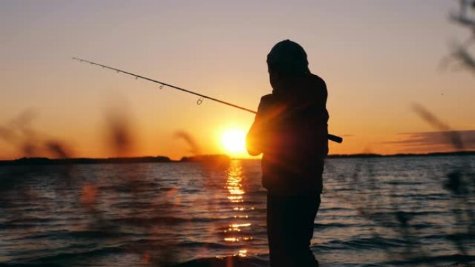 小男孩在日落时将钓鱼竿扔进湖中