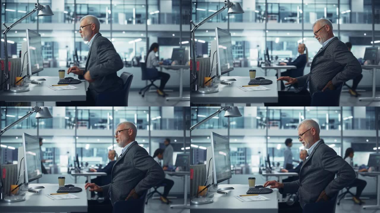 高级白人男性公司办公室工作人员在计算机上工作，突然感到背部疼痛。由于所有工作，压力，家庭问题，背痛，