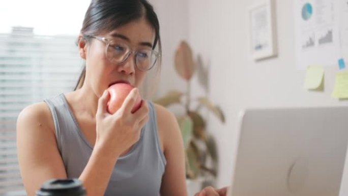 年轻女子吃健康的有机苹果看着笔记本电脑