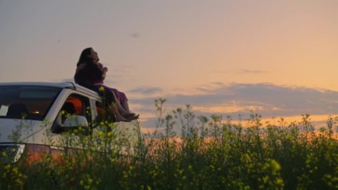 黄昏时分，两个女人抱在一起坐在一辆停在油菜籽地里的露营车的屋顶上
