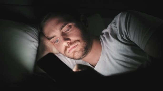 4k视频片段，一名男子晚上躺在床上时使用手机