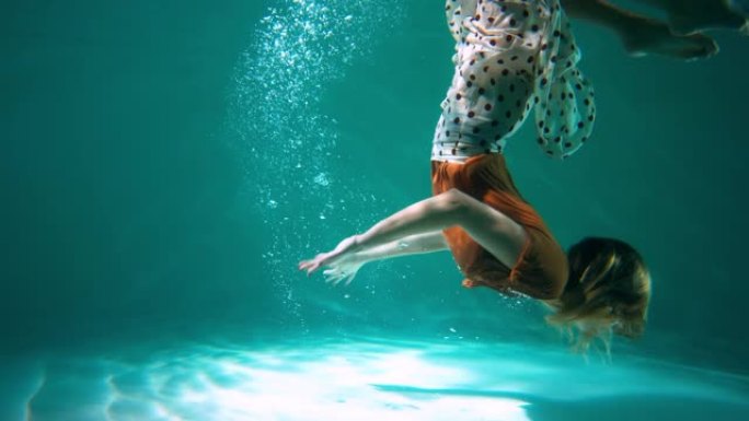 大气电影侧面拍摄的年轻美丽的舞者女人在浅蓝色的水慢动作下做后翻转动作。