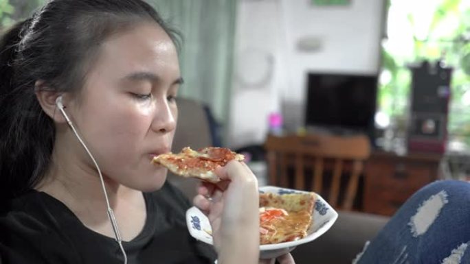 十几岁的女孩用耳机吃披萨，看智能手机