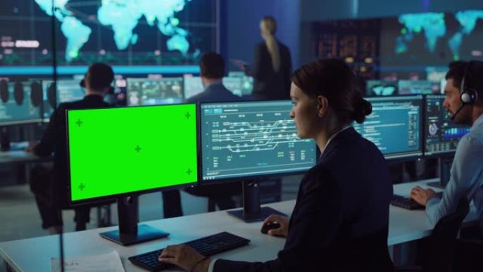 自信的女性数据科学家在大型基础设施控制和监控室中使用绿屏模型在个人计算机上工作。女工程师与同事在办公