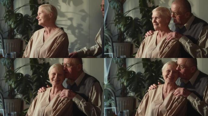 团结和爱。快乐浪漫的70年代高级丈夫拥抱美丽的白发妻子，在舒适的家庭厨房交谈。
