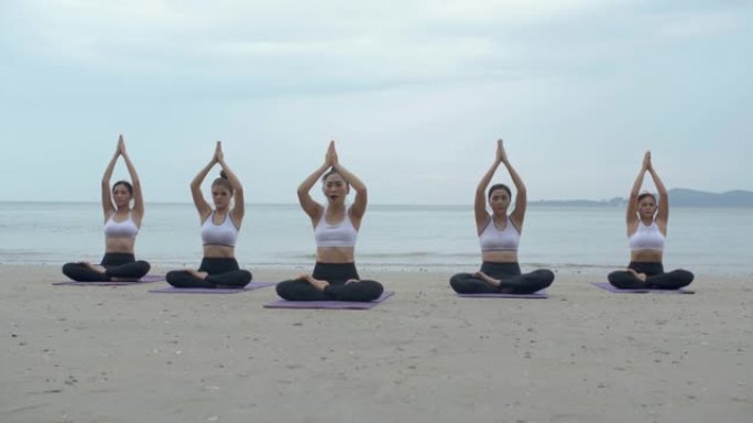 五人小组体育课在日出的早晨在海滩上一起练习瑜伽课。健身课程概念。