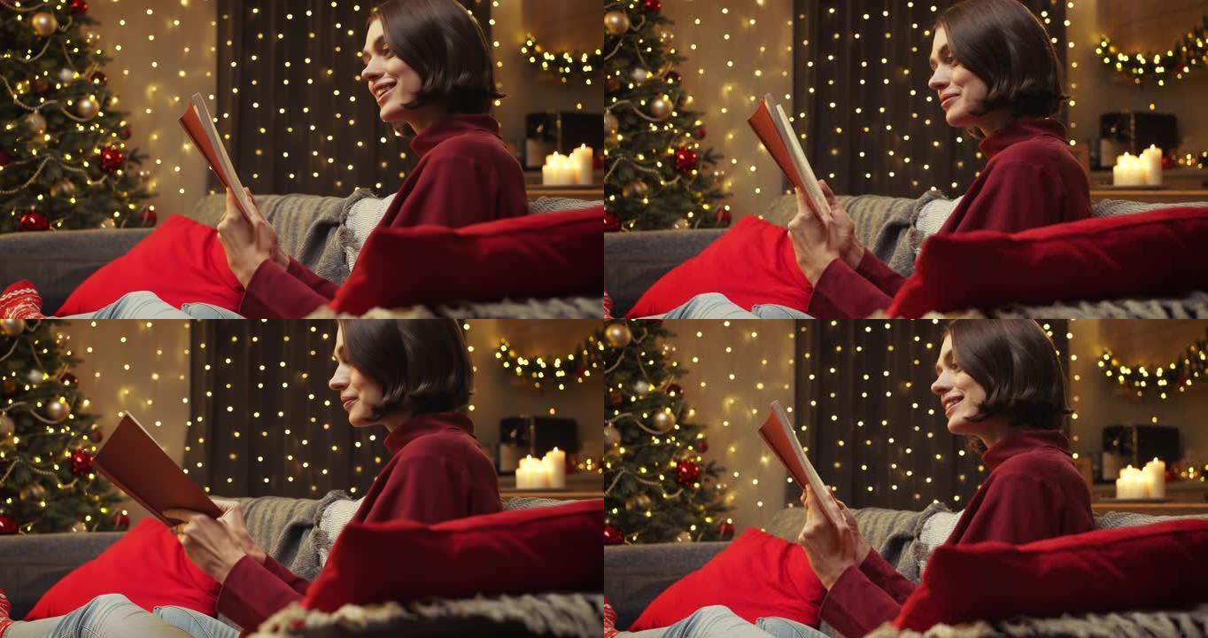 一位穿着红色毛衣的迷人年轻女子正笑着看书，坐在圣诞节室内的沙发上