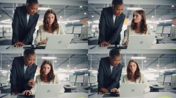 两名女同事深情地讨论工作，微笑着在各种现代商务办公室的笔记本电脑上展示项目。经验丰富的经理和年轻员工